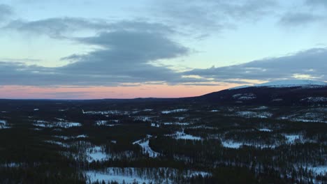 smooth drone flight over the snowy landscape of sweden with a light red glow at the horizon of the undergoing sun