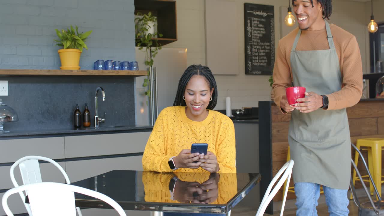 African American woman scrolling phone at cafe upon barista offering red mug, then smiling, sipping