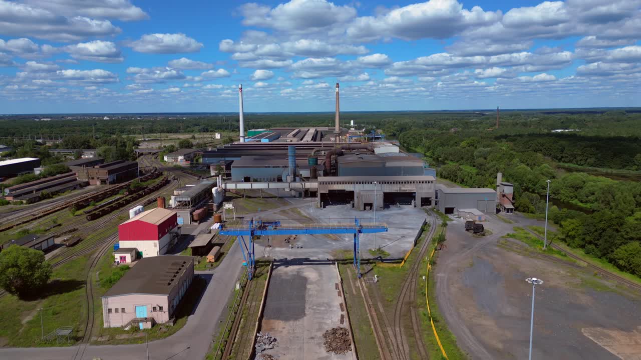 Hennigsdorf electric steel factory with train tracks, chimneys, and industrial buildings under a blue sky. Best aerial view flight descending drone