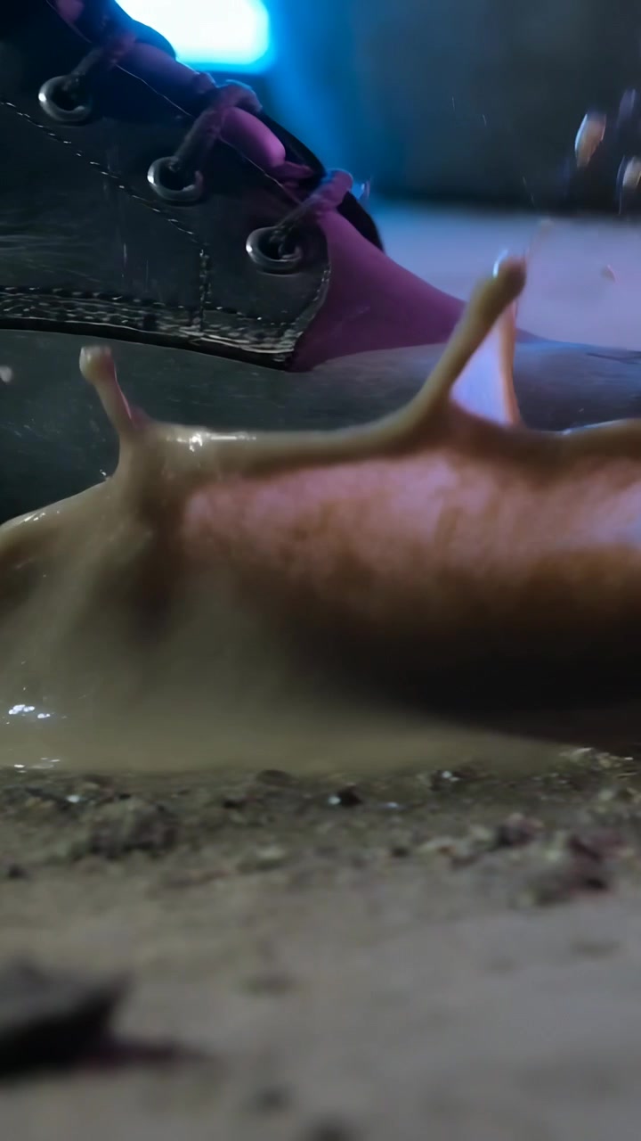 Vertical video: Stepping boot toe hitting puddle on wet ground while walking, sending mud, eyelets
