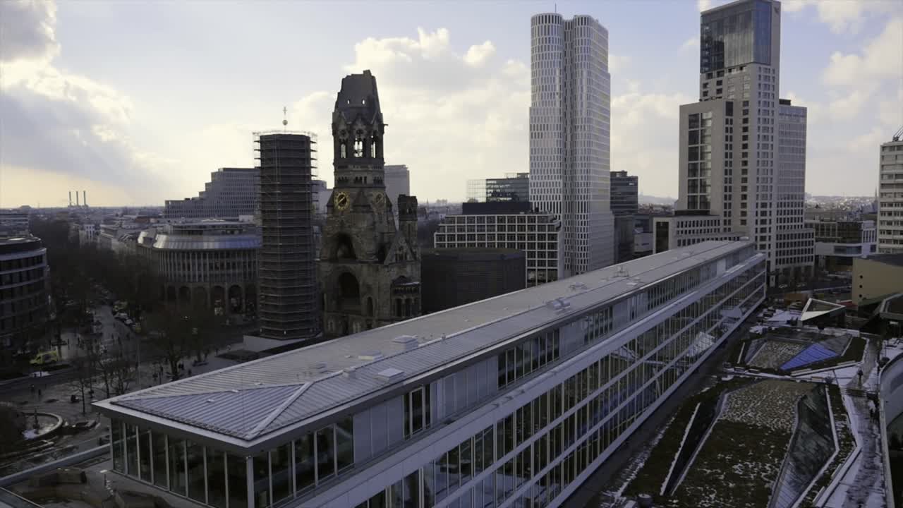 Kaiser Wilhelm Memorial Church stands with damaged spire beside modern high rises in central Berlin as winter highlights contrast between historic structure and surrounding contemporary skyline