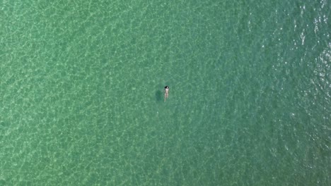 a young woman in a bikini swims on her back in the green waters of the aegean sea