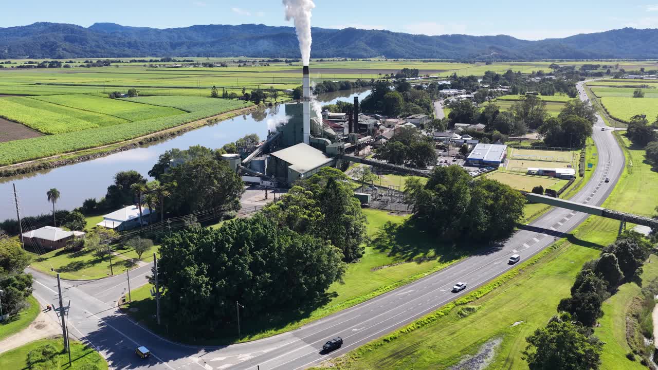 Drone footage captures a sugar mill surrounded by lush landscapes and a winding river under clear skies