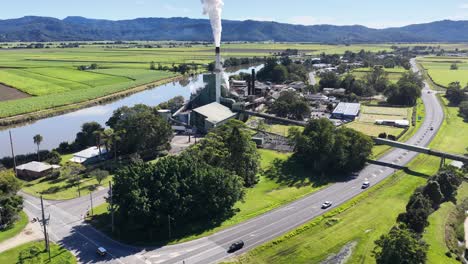 drone footage captures a sugar mill surrounded by lush landscapes and a winding river under clear skies