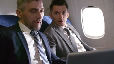 Businessmen-In-Suits-Talking-And-Working-On-Laptop,-Then-Shaking-Hands-And-Making-Deal-While-Traveling-By-Plane