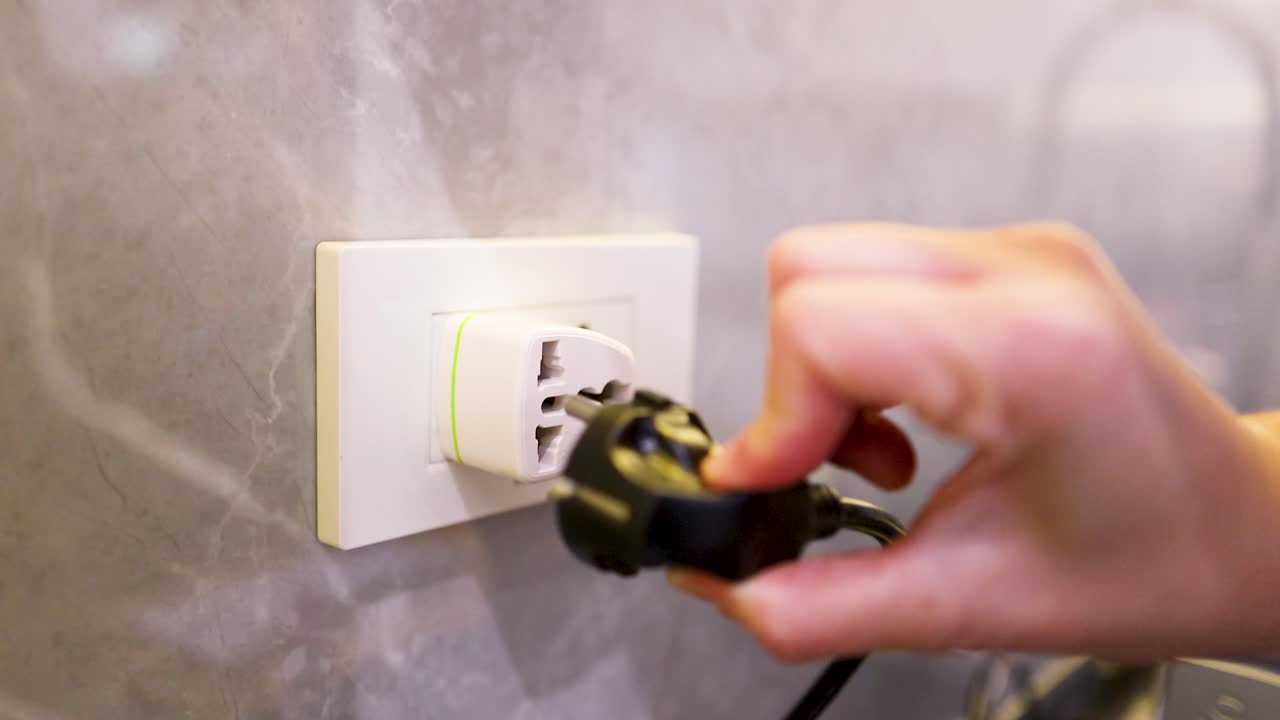 Close-up shot of a hand removing a black electrical plug from a white wall outlet