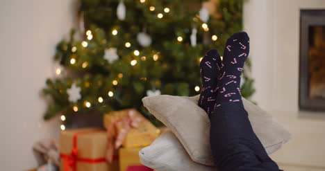 mujer relajándose con las piernas sobre cojines contra el árbol de navidad