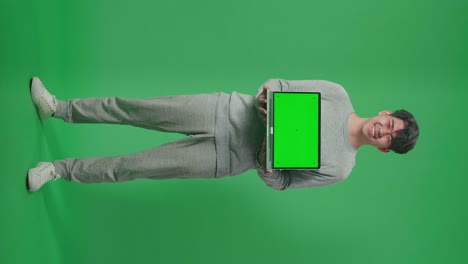 full body of smiling asian man holding green screen computer while standing in front of green screen background