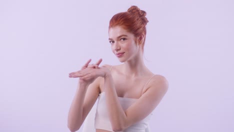 young fair-skinned redhead model gently applying hand cream in minimalist studio background.