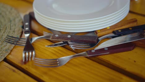 close-up of stacked white plates and wooden-handled forks and knives scattered on a yellow wooden table. daugavpils, latvia (latgale)