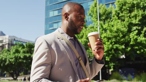 Glücklicher-Afroamerikanischer-Mann-In-Der-Stadt,-Der-Kaffee-Trinkt-Und-Sein-Smartphone-Benutzt