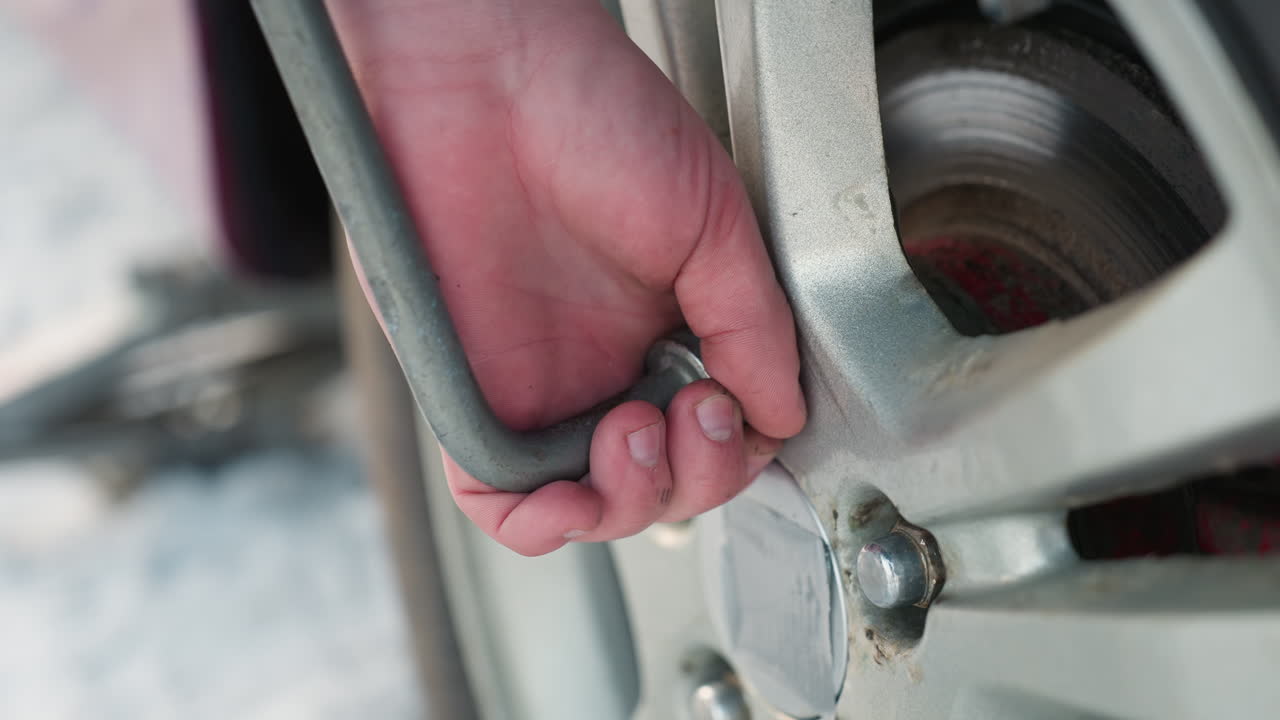 close up of person loosening car tire bolt rim with blurred snowy background, spanner in hand, winter scene, vehicle maintenance, focused action, cold weather, roadside tire repair