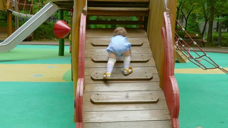 little baby girl struggling to climb wooden ladder at playground -back view