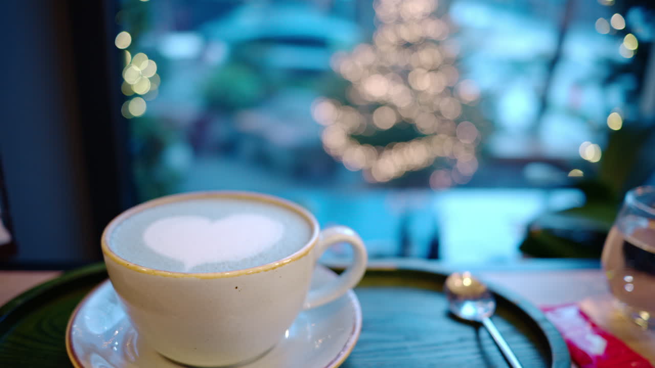 Cup of coffee with foam latte art in heart shape. Christmas tree on background
