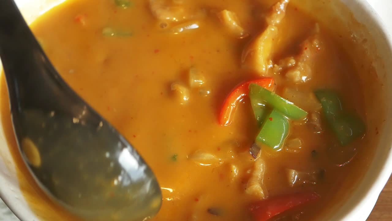 Primo piano di un cucchiaio che mescola delizioso curry con peperoni