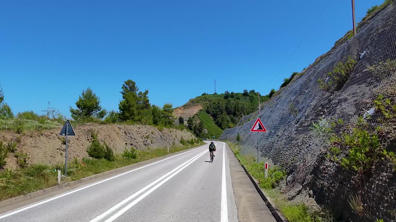 Beautiful Road Snaking Through Hills, Cyclist Riding Alongside Blue Lake on Scenic Route in Albania
