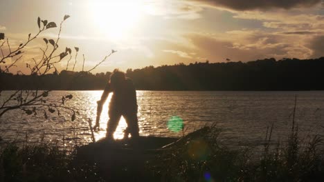 Young-man-beached-row-boat-puts-on-backpack-sunset