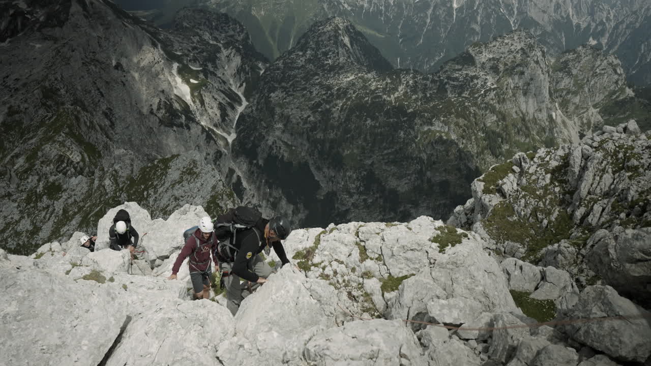 Um grupo de alpinistas escalando uma montanha com equipamento de escalada, em perspectiva aérea, com o vale visível ao fundo