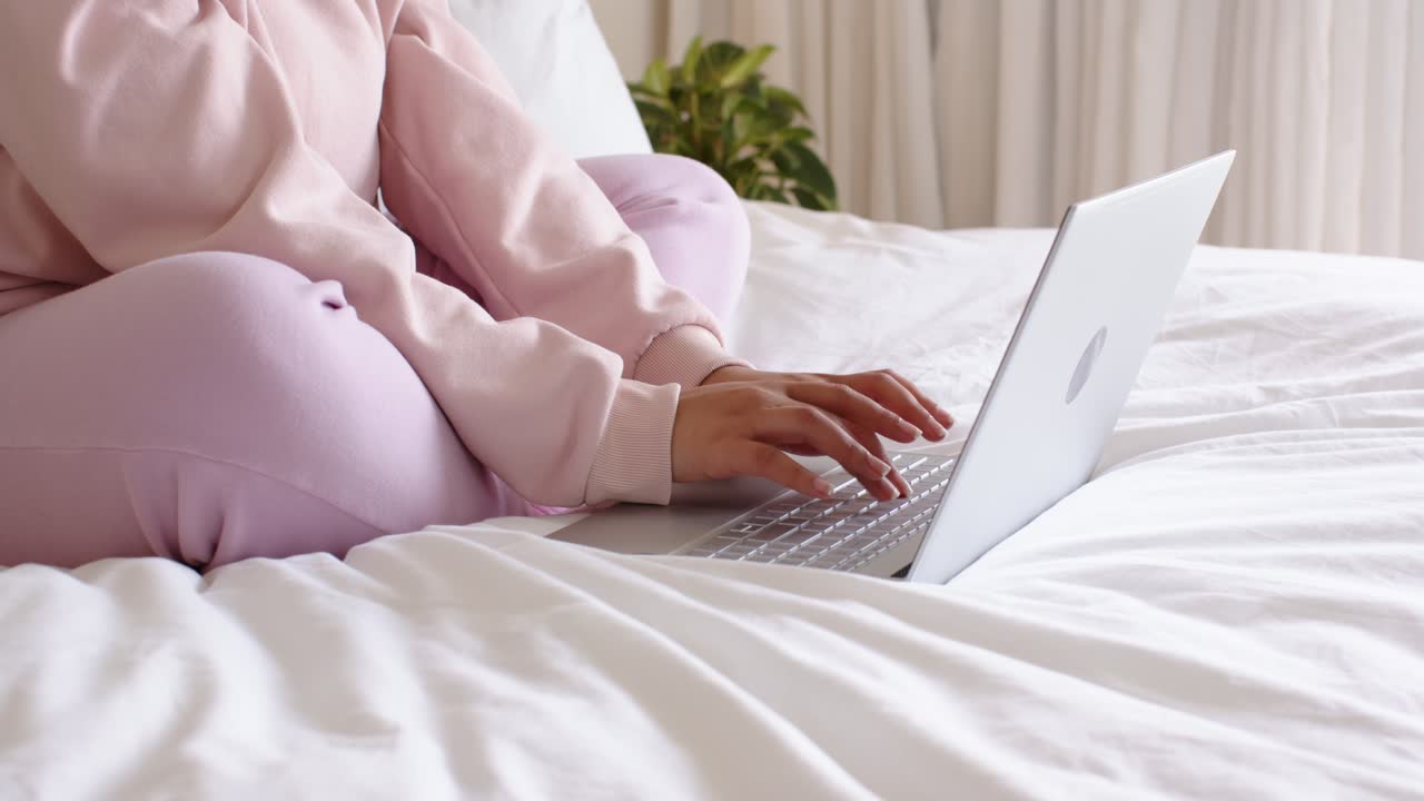 Eine Frau tippt auf einem Laptop im Bett, beginnt eine Arbeitssitzung und bewegt ihre Handgelenke in der Nähe einer Pflanze