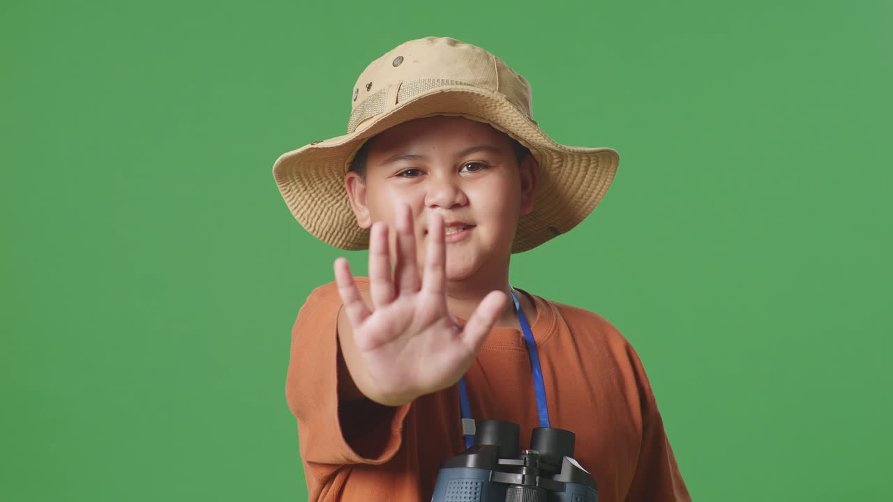 모자와 안경을 가진 아시아 관광 소년은 보기를 사용하며, 녹색 화면 배경에 서있는 동안 손을 표시하지 않습니다. 소년 연구자, 여행 관광 모험, 클로즈업
