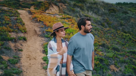 romantic couple going hill looking on cloudy landscape. pair walking grass slope