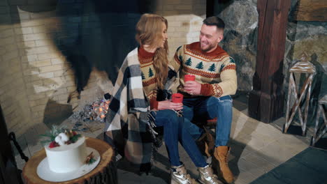 beautiful loving couple resting near fireplace. young woman and a man with cups. guy is hugging girlfriend and enjoying romantic weekend.