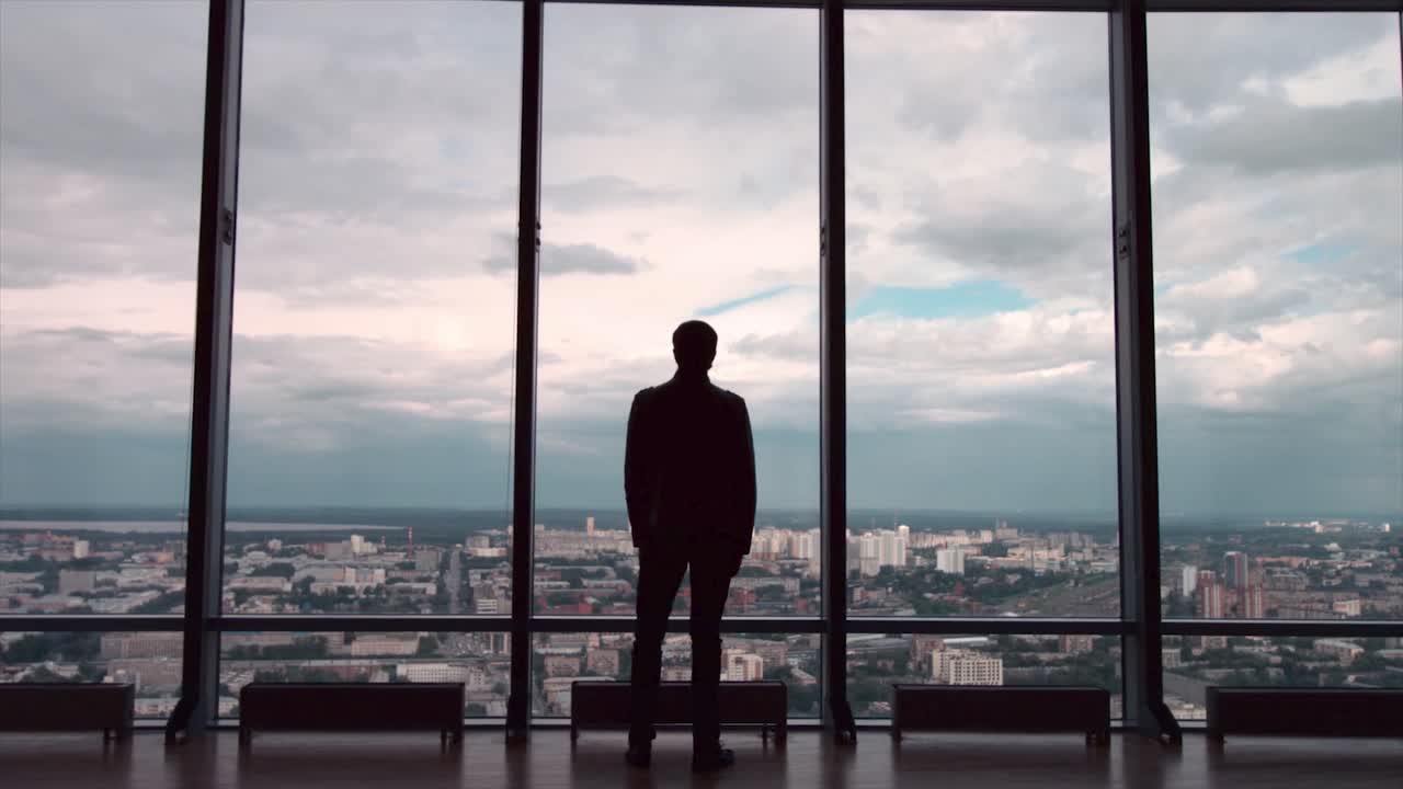 un hombre de negocios contemplando el paisaje de la ciudad desde una ventana de gran altura.