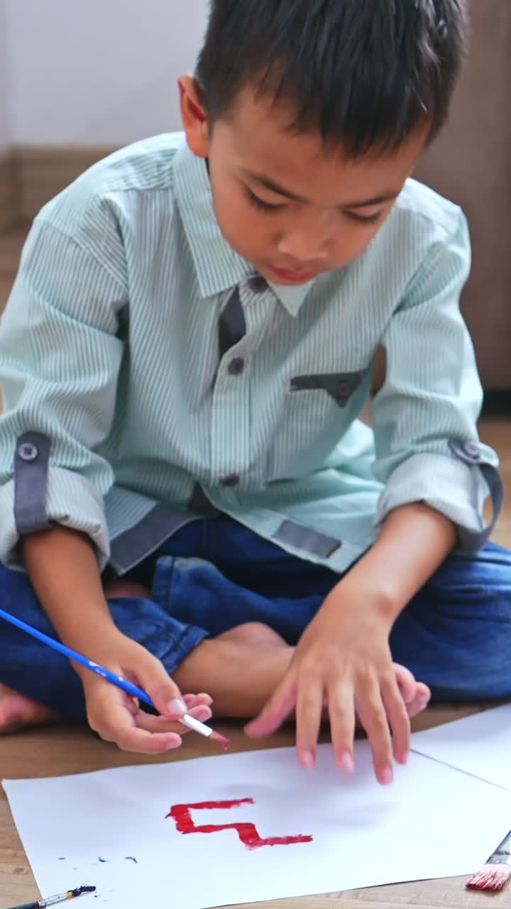 Young asian boy focused on painting red lines on white paper