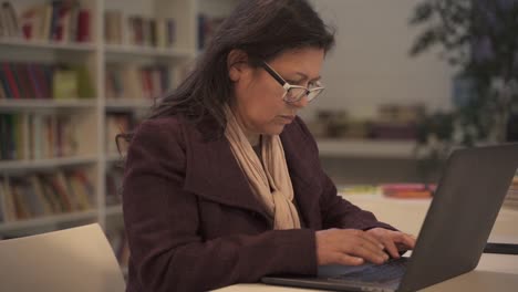 Encantadora-Anciana-Escribiendo-En-Un-Ordenador-Portátil-En-La-Biblioteca-De-La-Universidad,-De-Cerca