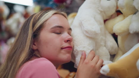 lady in pink dress rests her head on a soft white toy in a toy store, smiling gently while feeling the texture, surrounded by other plush toys on the shelves, she removes her head from the toy