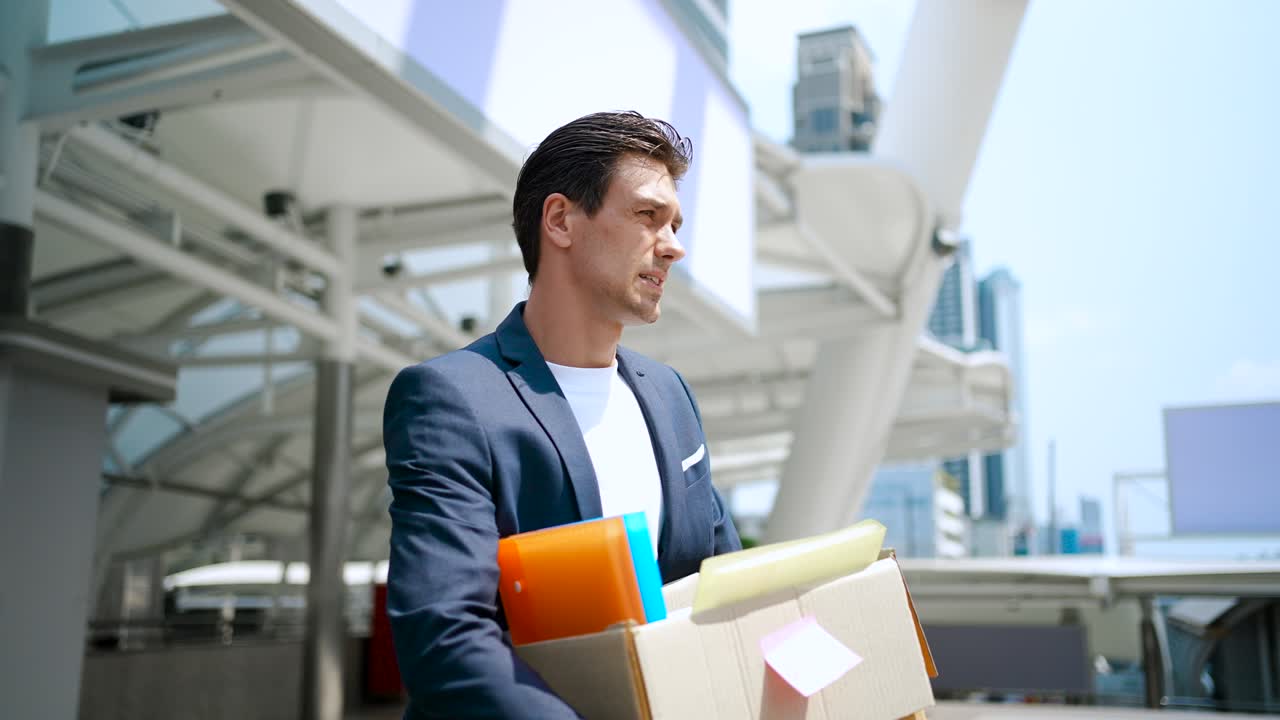우울한 사업가가 회사에서 해고되고 개인 물건의 상자를 운반하고 있습니다.