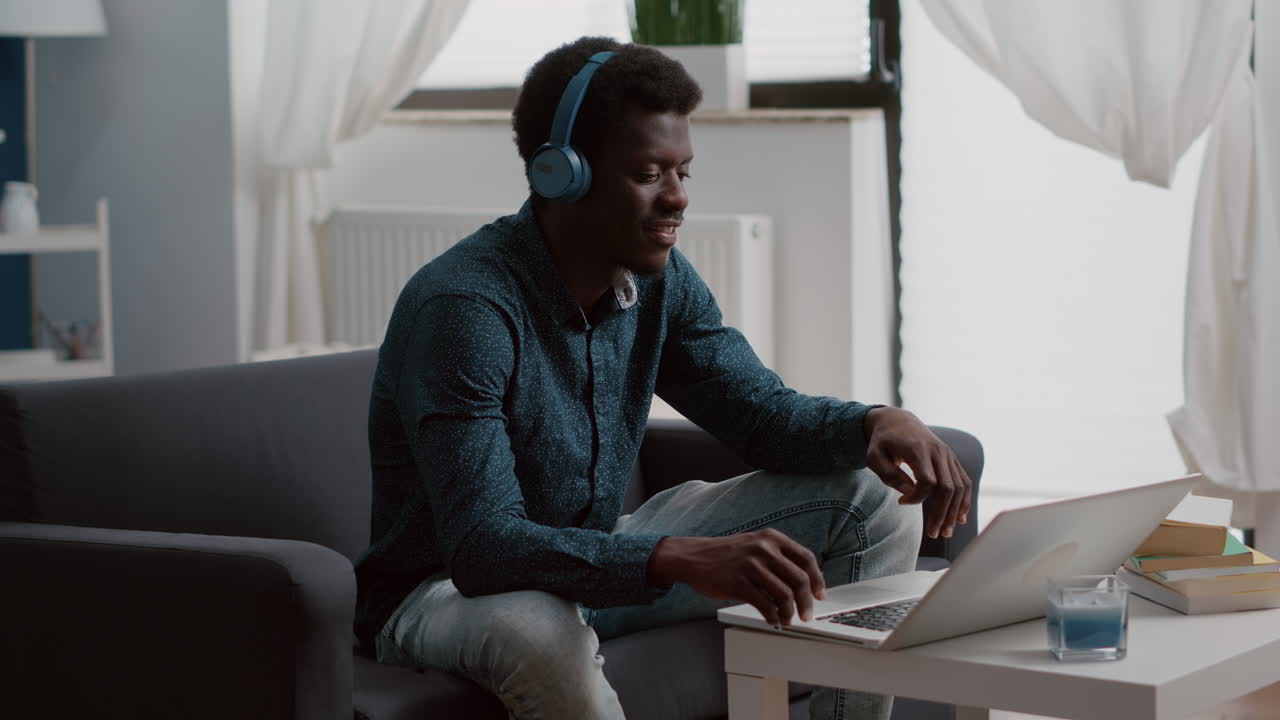 Authentic smiling african american man using laptop with headphones on, working from home