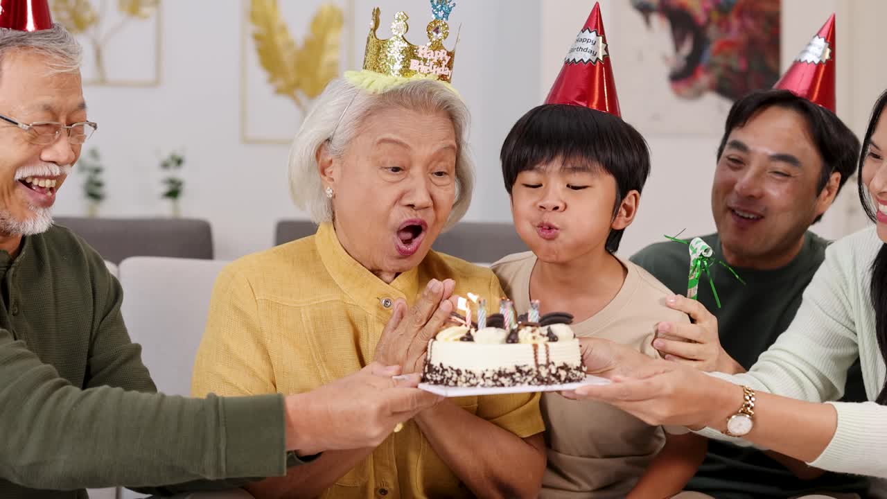 高齢の家族と子供たちが、温かい家庭の雰囲気の中で、ケーキ、ろうそく、笑い声と共に楽しい誕生日パーティーを楽しむ。