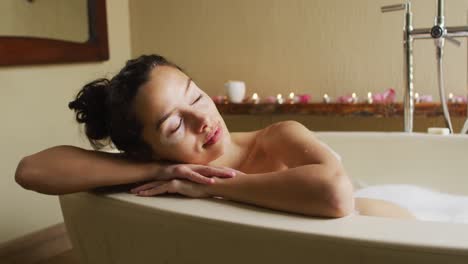 relaxed biracial woman with vitiligo relaxing in foam bath with candles pampering herself