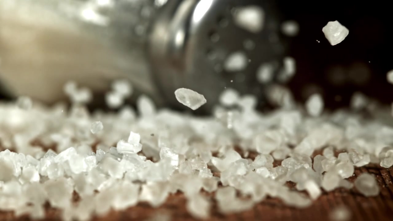 Groft havsalt falder i slowmotion ned på en træoverflade