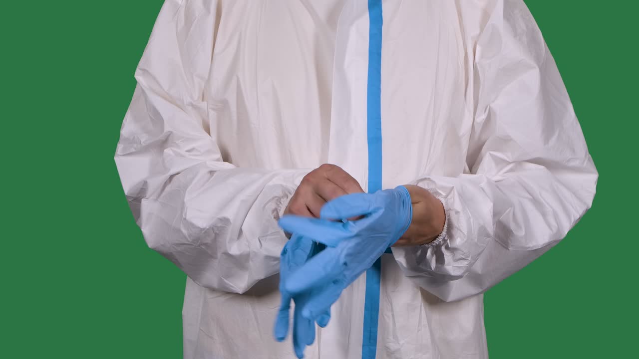 trabajador médico profesional en un traje de protección blanco se pone guantes quirúrgicos azules. torso y manos hombre de cerca. pantalla verde, llave de croma. cámara lenta