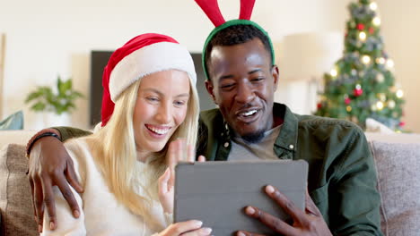 christmas time, diverse couple enjoying holiday video call on tablet at home, smiling together