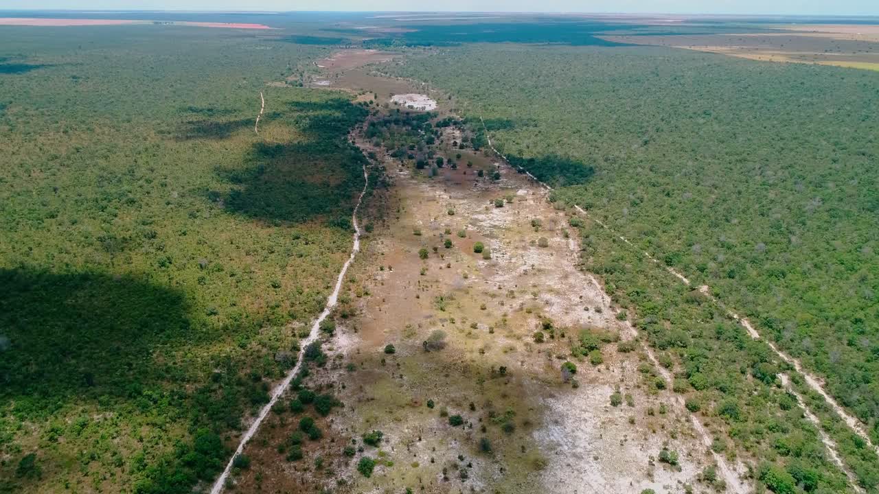 Lento avvicinamento aereo con drone di un sito di ripristino del bioma del Cerrado che mostra un alveo sabbioso e asciutto fiancheggiato dal tipico mosaico di vegetazione della savana, struttura di gestione bianca, geomorfologia dell'altopiano