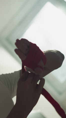 el atleta protege la mano con un envoltorio para el boxeo en el gimnasio de combate. el boxeador pensativo aplica una tira de tela para la palma y la muñeca en el club de artes marciales en cámara lenta