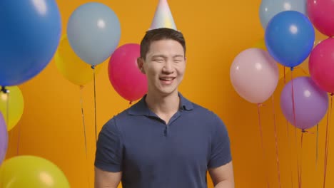 retrato de estudio de un hombre con sombrero de fiesta celebrando su cumpleaños con globos y soplador de fiesta 2