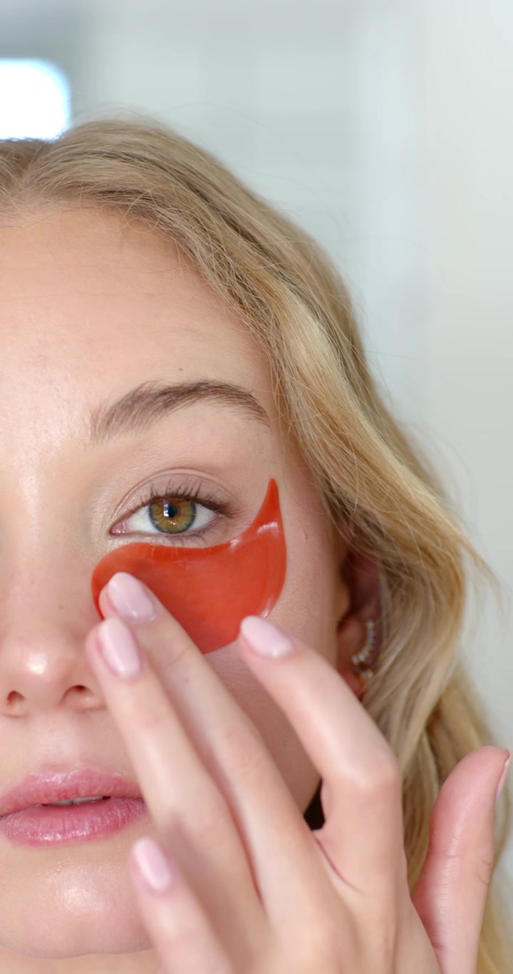 Vertical video: Woman picking red eye patch applying under left eye with fingers at home for skin