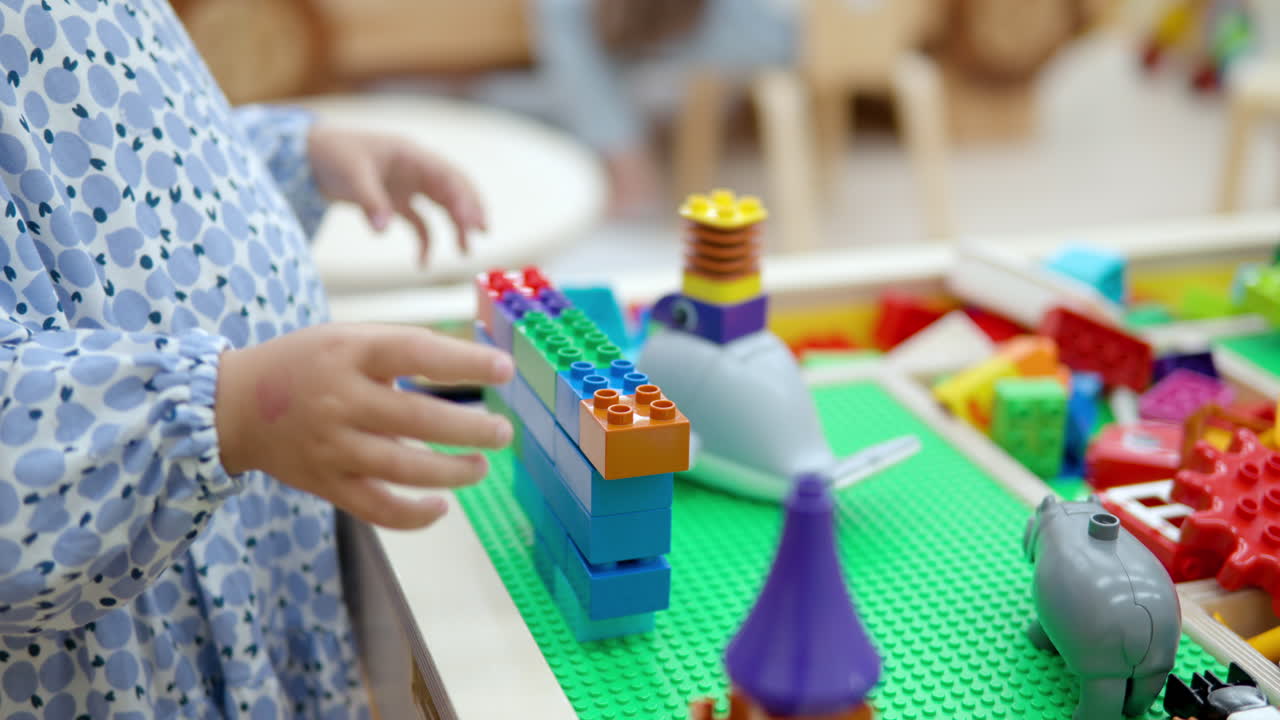 niña pequeña jugando a construir una pared con ladrillos o bloques de lego - manos en primer plano