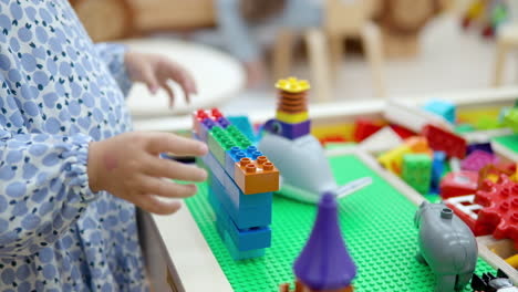 child little girl playing constructor building wall with lego bricks or blocks - hands close-up