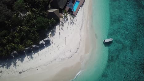 Serenity-island-exotic-paradise-resort-destination,-bird-view-flying-over-top-of-tourist-boat-on-turquoise-coral-reef-ocean-and-the-resort