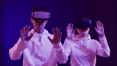 Asian-man-and-woman-using-vr-headsets,-touching-virtual-screen-on-blue-background,-slow-motion