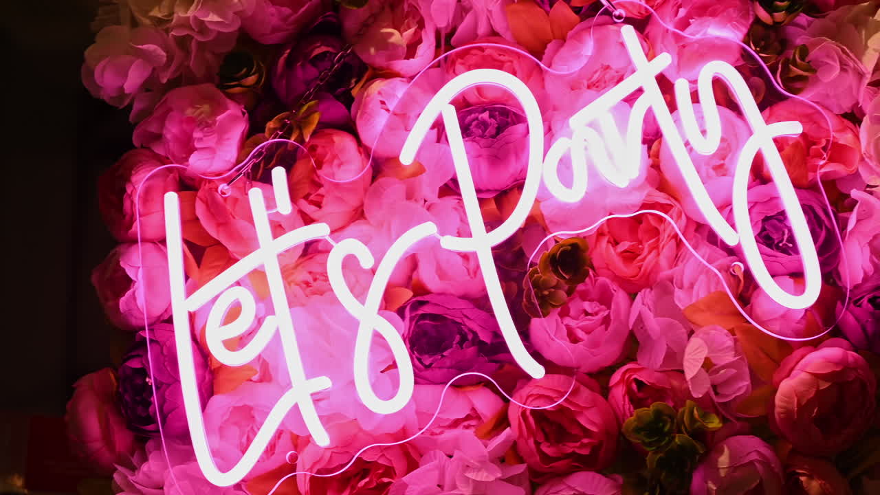 Lad os feste: lysende neonpink skilt med blomster i baggrunden