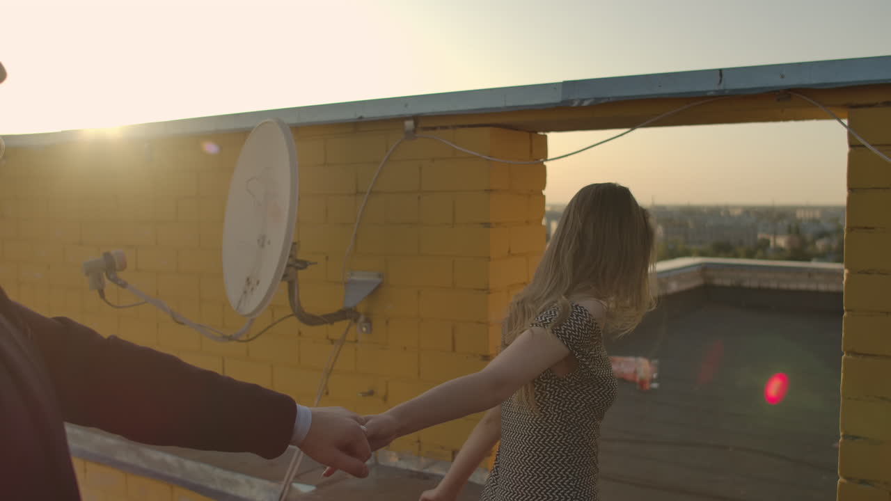 Cute lovers laughing running on the roof of the building at sunset on the background of the city and hugging standing at the edge. Romance and love