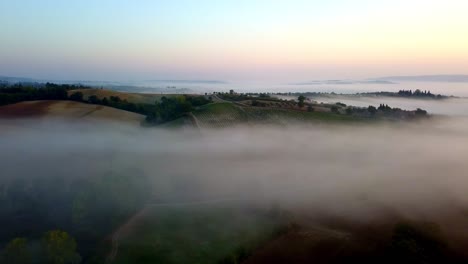 sunrise with tuscan countryside fields in italy on a cold fog filled morning, aerial left pan lowering shot