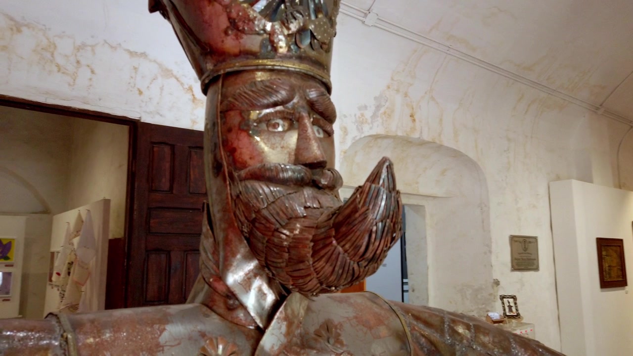 Primo piano di una statua in legno intagliato e barbuta che indossa una corona all'interno di un edificio storico in Messico, con dettagliate caratteristiche facciali, barba, veste e una lavorazione artigianale ornata.