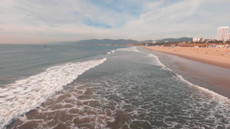 the beautiful santa monica beach with waves rolling to the shore and mountains in the distance - wide shot